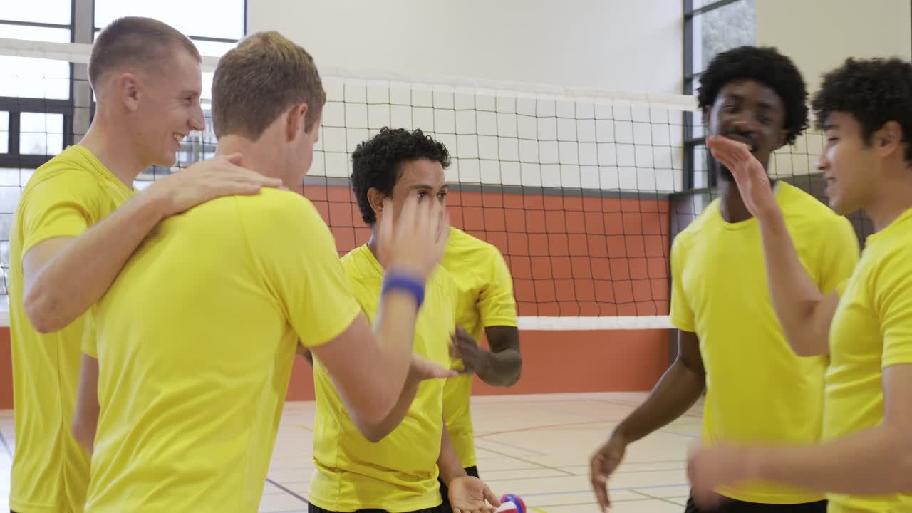 Squadra maschile di pallavolo multietnica in magliette gialle che si stringe in cerchio, si incita e si abbraccia alla rete dopo un punto.
