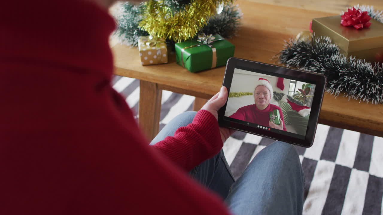 Uomo caucasico che usa il tablet per una videochiamata di Natale, con un amico sorridente sullo schermo.