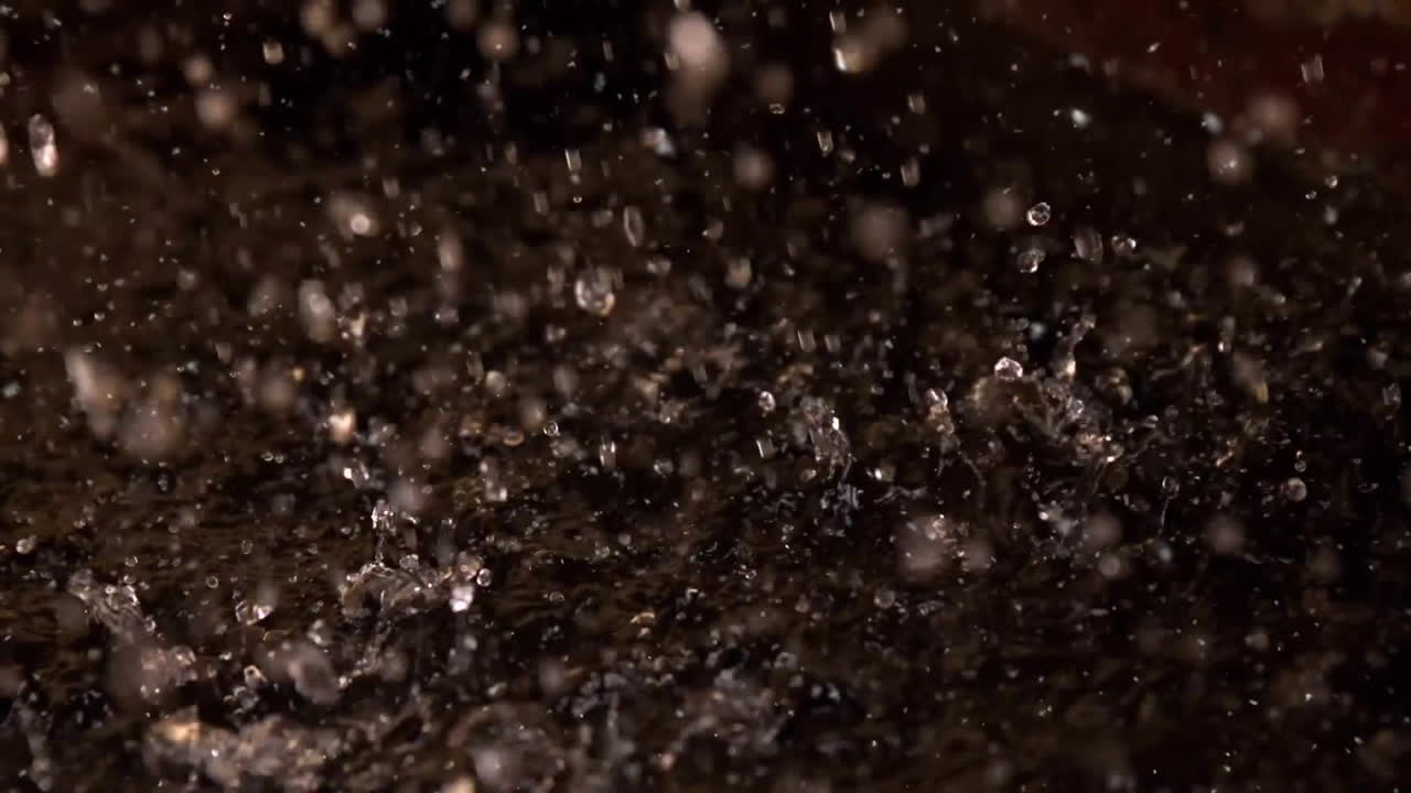 Animazione di gocce di pioggia che schizzano su superficie scura, creando increspature e goccioline