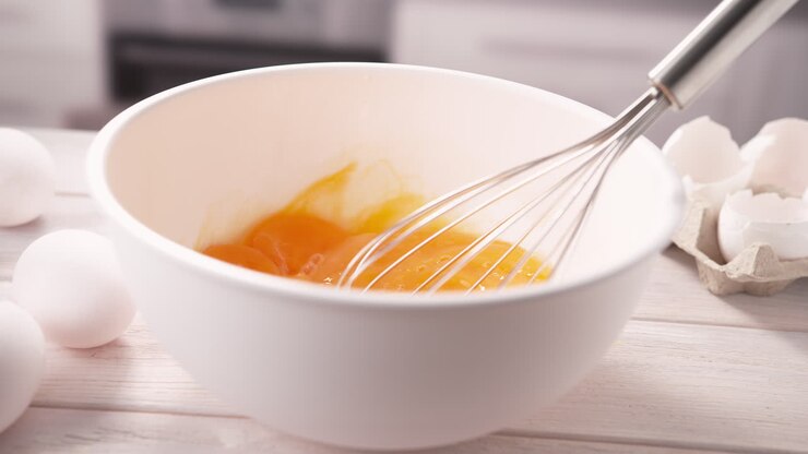 Whisking Eggs For Omelette In A White Bowl With Egg Beater - Preparing Breakfast in Slow Motion