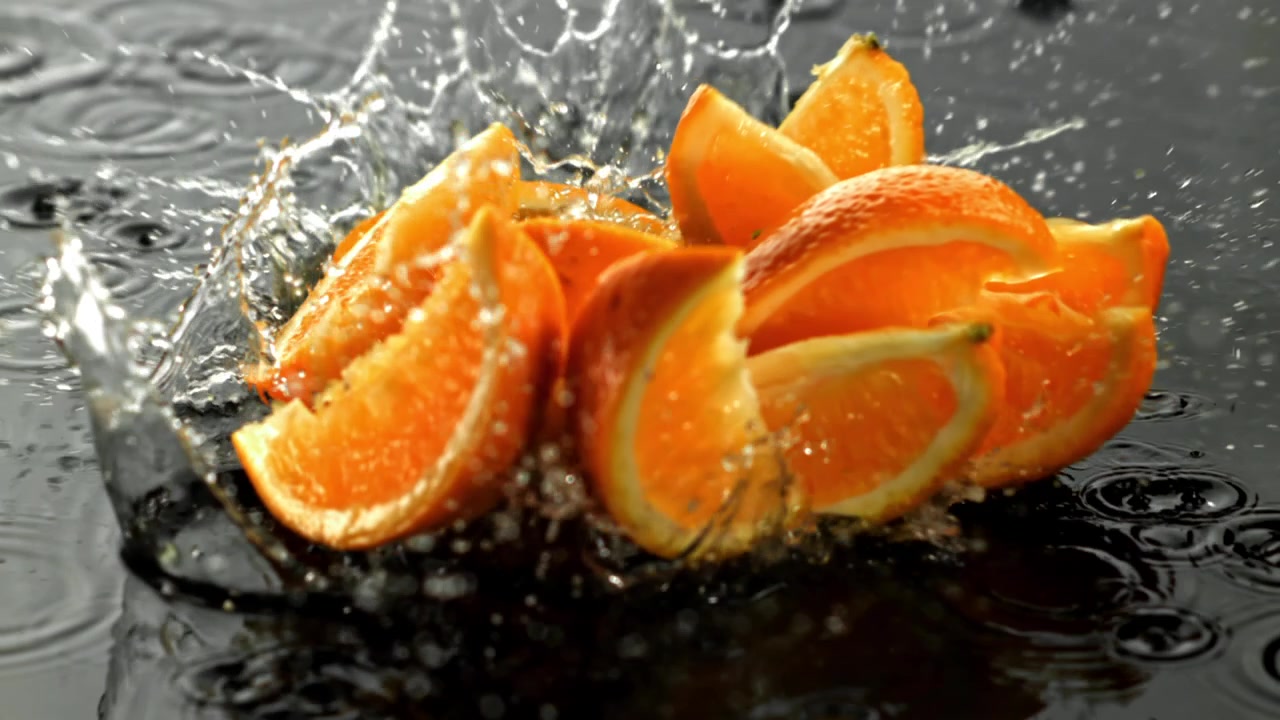 Fette d'arancia che cadono e schizzano nell'acqua al rallentatore.