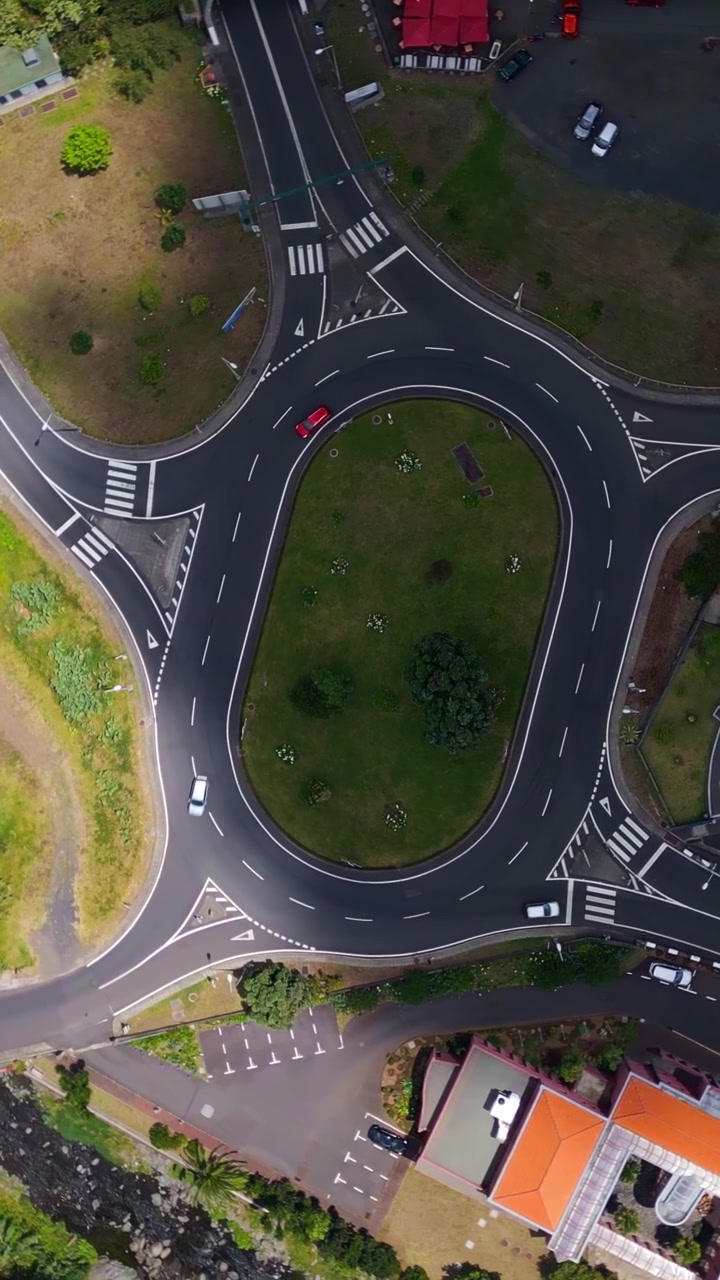 Roundabout with various exits and landscaped traffic island in São Vicente, Madeira, Portugal with marked lanes, crossings and light vehicle movement, vertical aerial view