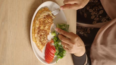 Person eating an omelet with fresh salad for a meal