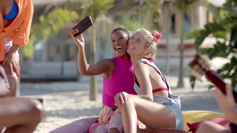 Fröhliche,-Vielfältige-Gruppe-Von-Freunden,-Die-Am-Strand-Mit-Strandhaus-Selfies-Machen-Und-Gitarre-Spielen