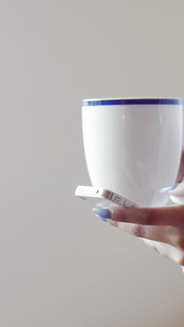 mujer usando el teléfono móvil mientras toma una taza de café