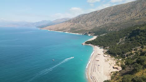 panoramic aerial overview of tropical white sand beach as boat drives along up to shore