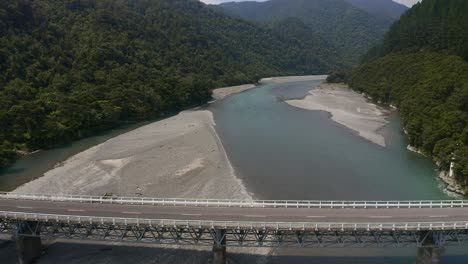 aerial: flying backwards down the motu river and over the highway 35 bridge with cars driving over