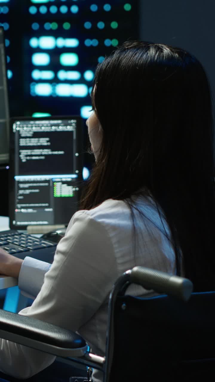 Donna in sedia a rotelle che programma al computer in un ufficio buio