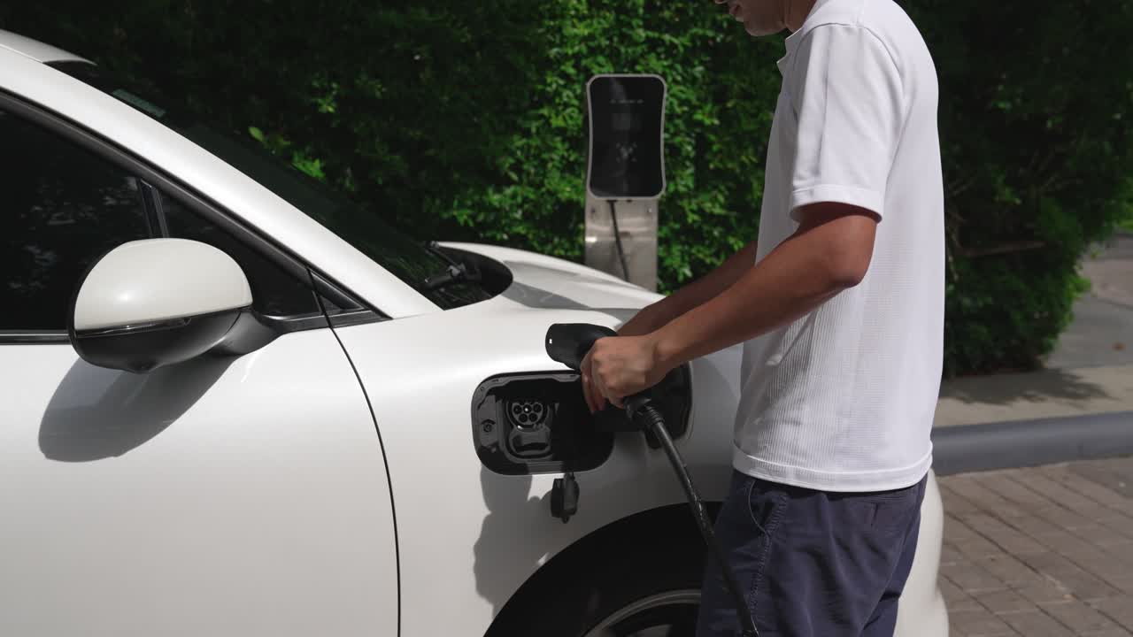 Ev şarj istasyonundan elektrikli aracına (EV) şarj kablosunu takan ilerici adam.