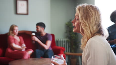 Young-blonde-woman-sitting-in-a-pub-holding-a-drink-and-talking-to-an-unseen-friend,-close-up