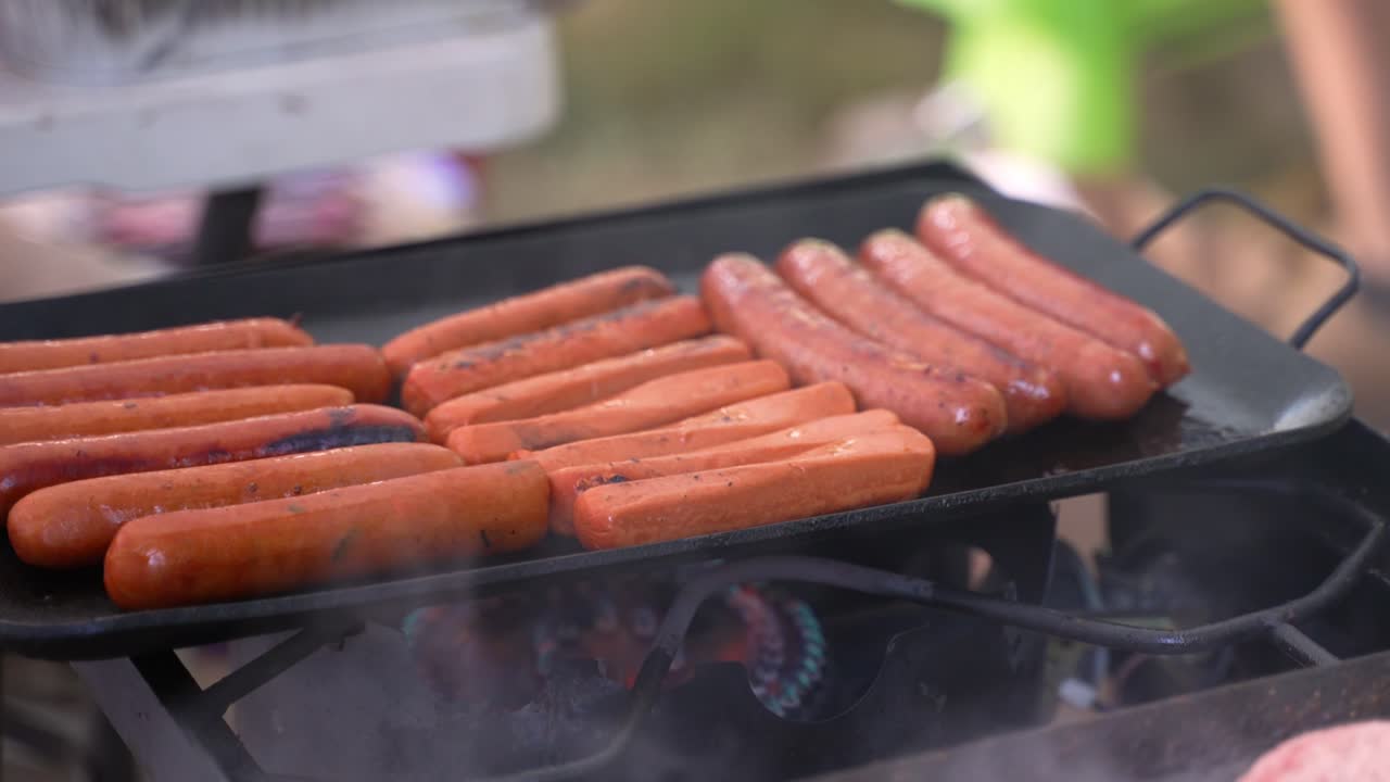 perros calientes carne carne de res cerdo y salchichas vegetarianas a base de plantas vegetarianas cocinadas en una parrilla de sartén de hierro fundido en el campamento, tiro apretado con humo soplando en el viento