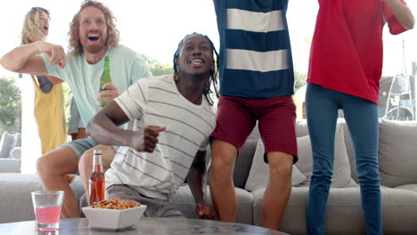 excited diverse friends with drinks watching sport on tv and celebrating, slow motion