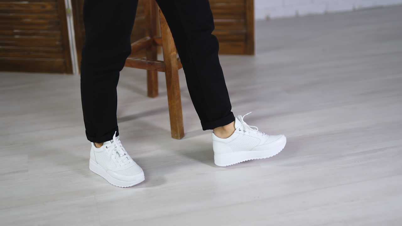 Fashionable white comfortable shoes presentation. Lady demonstrating beautiful footwear walking in the studio.