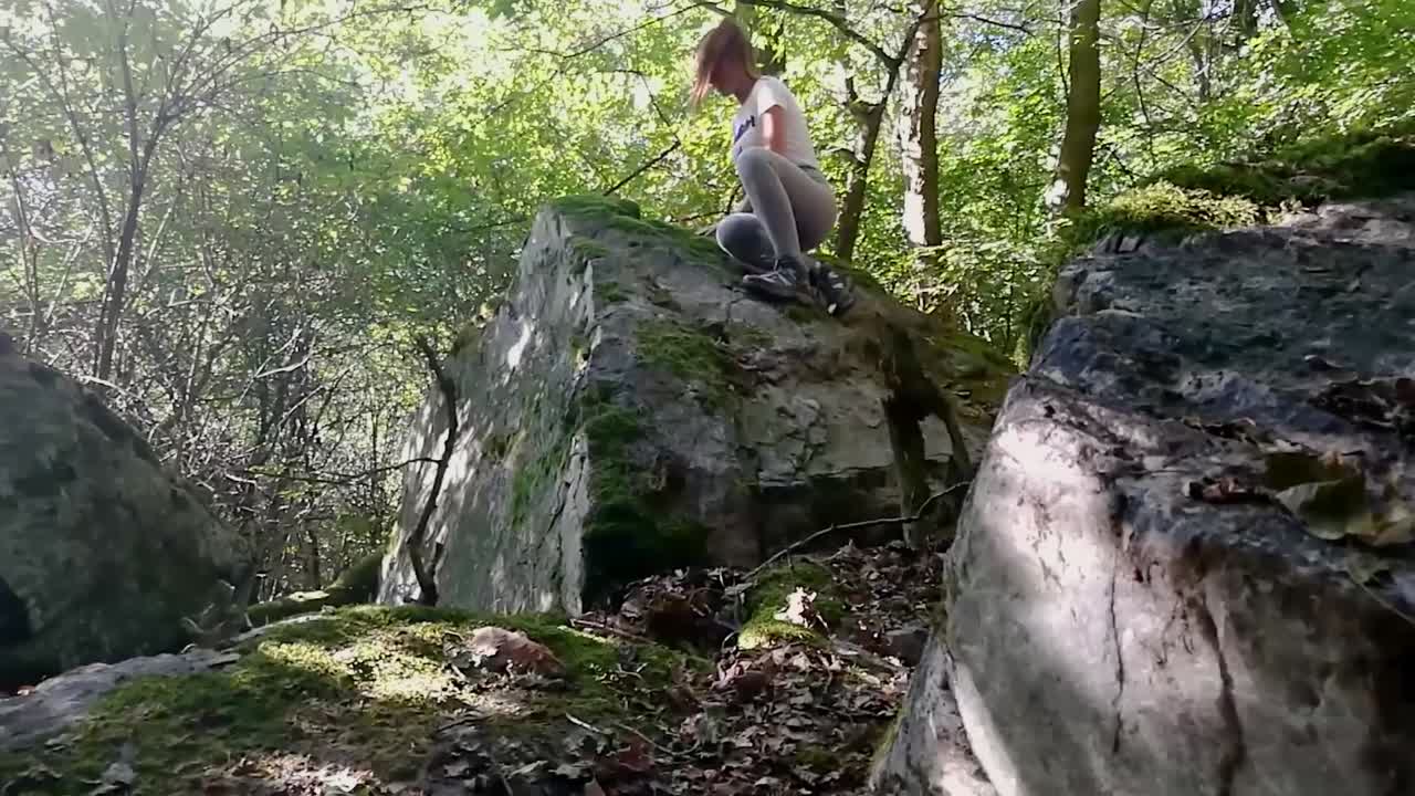 niña con cola de caballo marrón trepando en una gran roca en un bosque profundo en un día de finales de verano, slomo