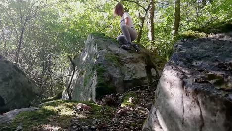 Young-girl-with-brown-ponytail-climbing-on-a-big-rock-in-deep-forest-on-a-late-summer-day,-SLOMO