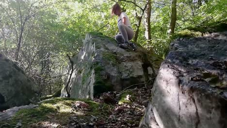 niña con cola de caballo marrón trepando en una gran roca en un bosque profundo en un día de finales de verano, slomo