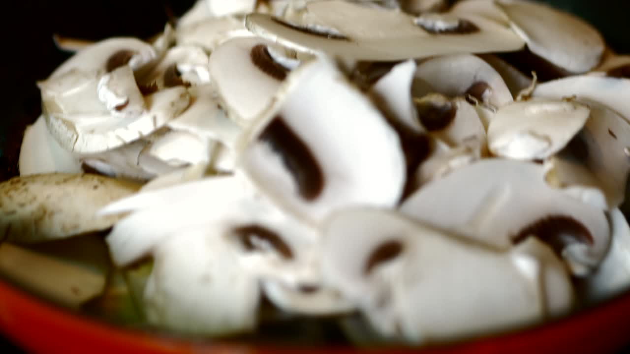 los champiñones en rodajas se fríen en una sartén roja caliente