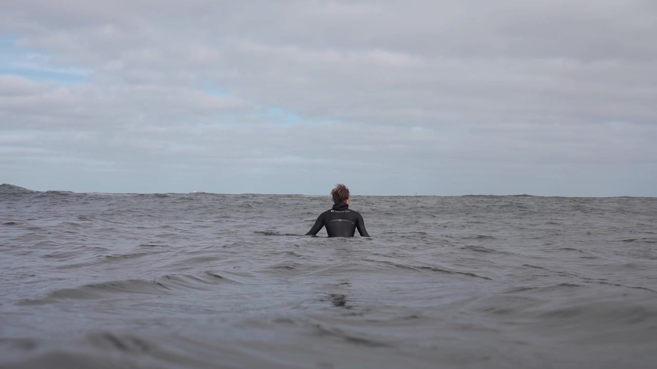 Solo surfer in wetsuit floating amidst vast endless sea