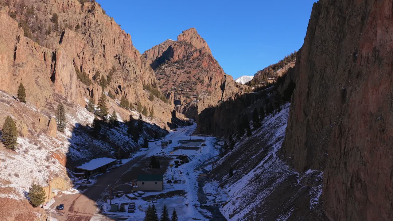 A cinematic aerial view captures the dramatic contrast between deep canyon shadows and a sunlit mountain peak. Steep rocky walls and rugged textures define the immense scale of this Southwest terrain