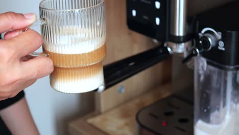 hand holding a latte art glass cup with coffee machine in background