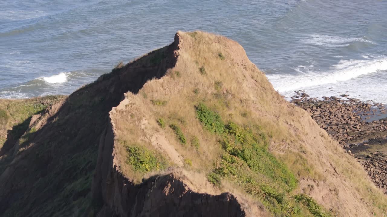 aerial drone footage of Knipe point over Cayton Bay with blue sky and ocean and big waves