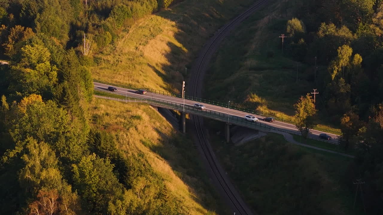 Aerial tilt down and zoom in to bridge as cars cross road outside of Augsligatne, Latvia, featuring lush forests and rolling hills
