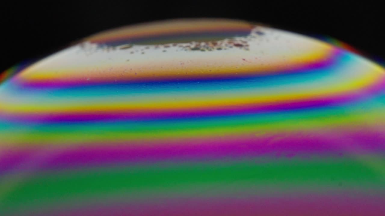 Vivid rainbow colors swirl across a bubble's surface in a mesmerizing close-up shot