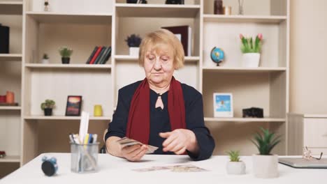 older, sad woman discontentedly counts dollar bills, arranging them on the table
