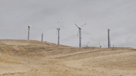 group of windmills on dry hill, some broken, as clouds slowly drift by