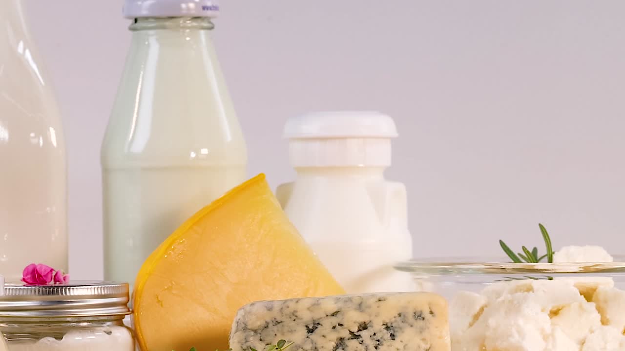 A variety of cheeses and milk bottles arranged with decorative elements on a neutral background.