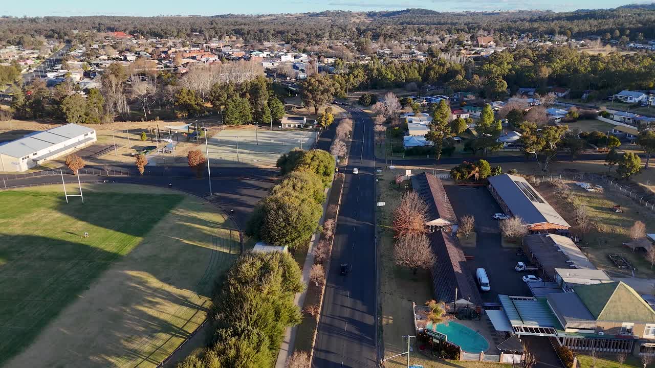 Drone footage follows a car driving along a quiet residential street in a small Australian town, with late afternoon sunlight and clear urban details