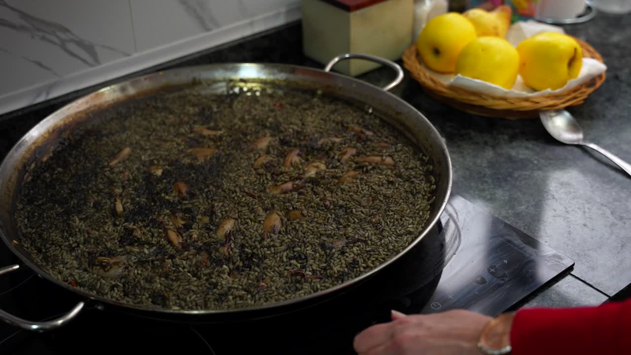 mujer agita la olla con paella, arroz negro y tinta de calamar