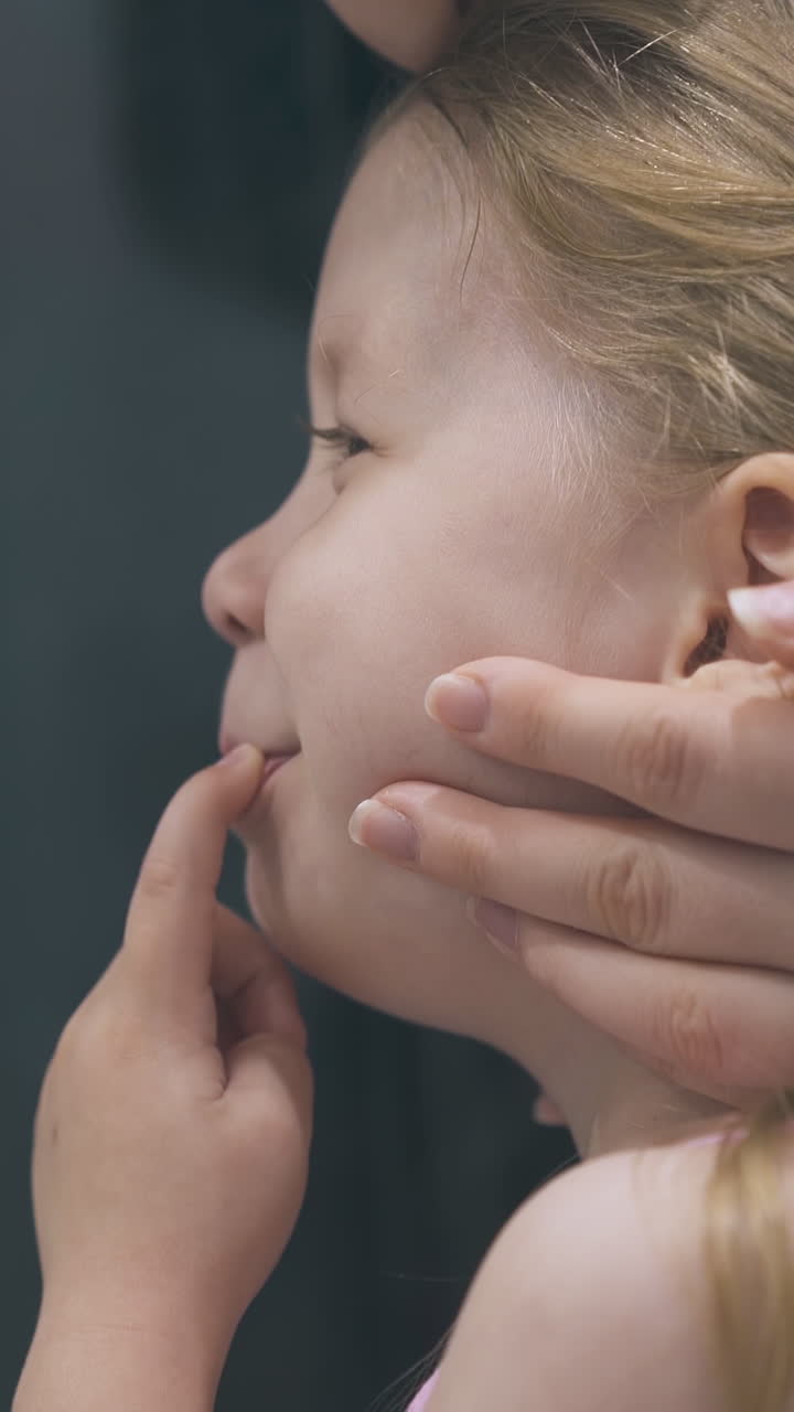 careful mother strokes pretty little girl fixing long hair in bathroom on blurred background close side view
