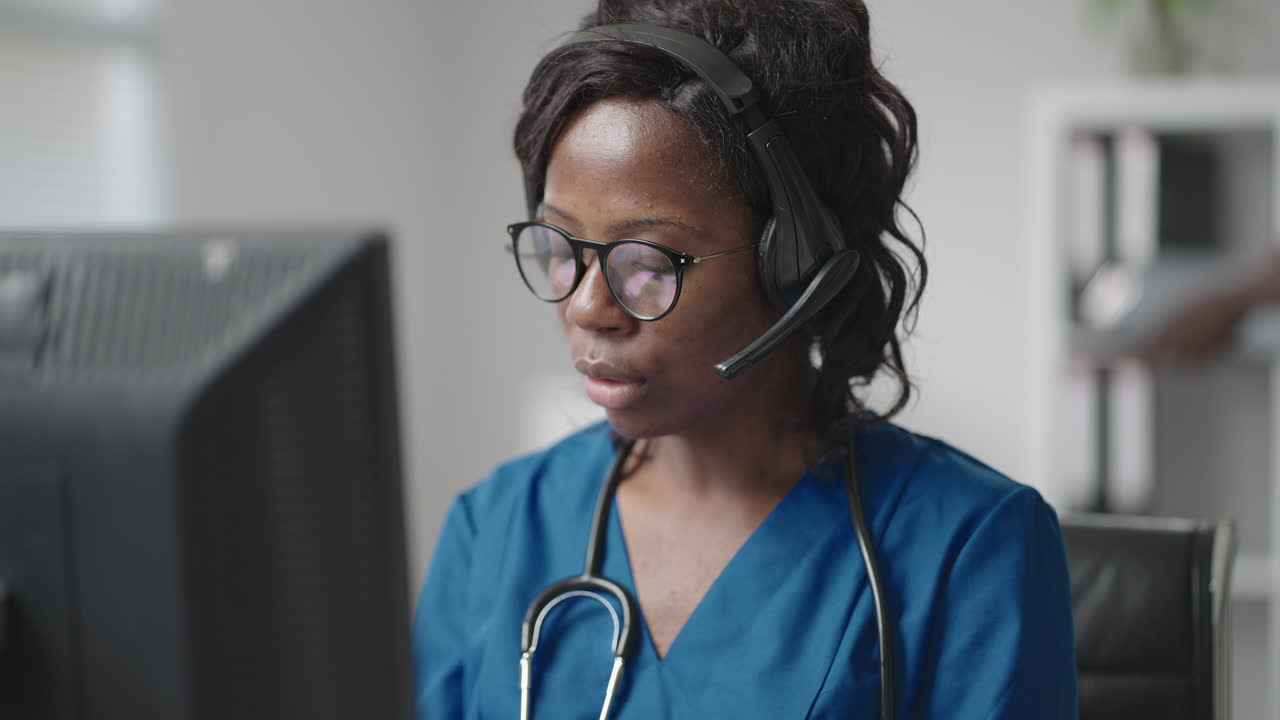 African american black female general practitioner in white coat sitting at desk in doctor's office and scrolling computer mouse while reading patient's medical history