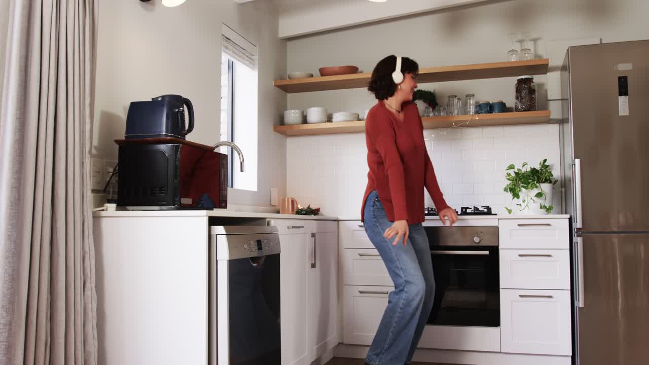 Donna che si sistema le cuffie e balla in cucina ascoltando musica con una macchina da caffè e delle tazze, spazio per la copia