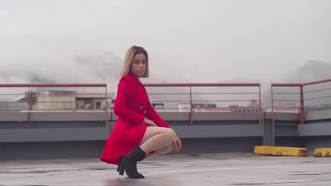 Atop-a-city-rooftop,-a-young-Hispanic-girl-dons-a-short-red-dress-while-in-a-squat-position