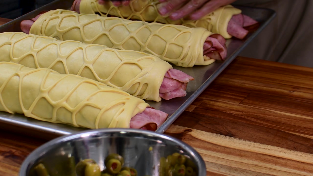 Preparing ham roll with olives, bacon, and raisins on wooden board
