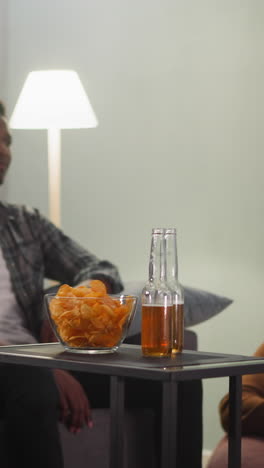 black man puts bottles of cold beer onto table to watch baseball game with friends at home closeup slow motion. happy sports fans men and women at broadcast