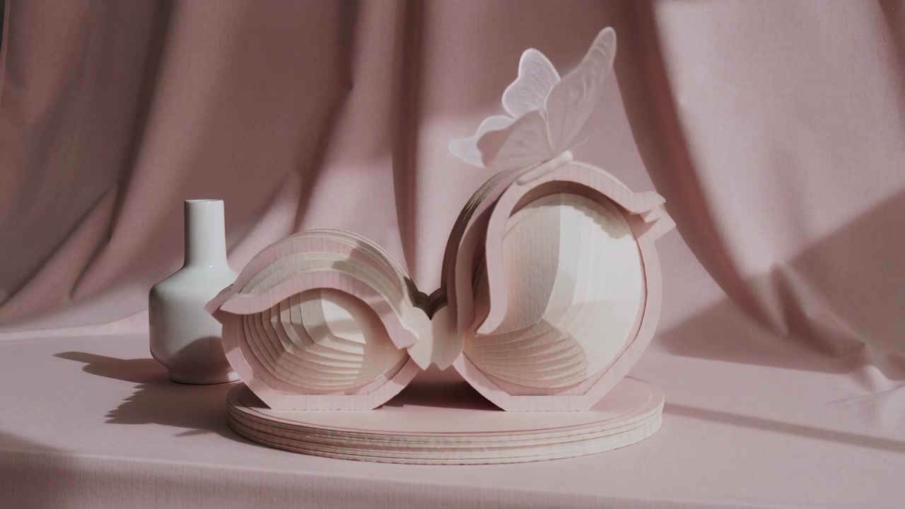Appearing paper butterfly fluttering above ring sculpture and white vase at studio