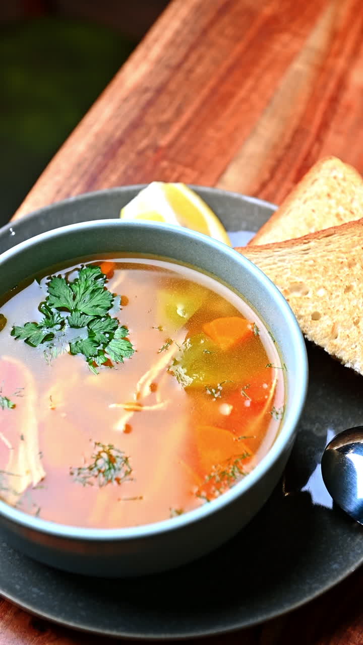 Varm hønsekødssuppe med grøntsager og toast serveret på tallerken. Klar hjemmelavet hønsekødssuppe med grøntsager og urter serveret med ristet brød på grå tallerken