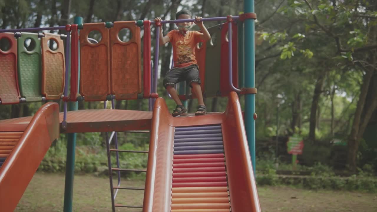 un niño pequeño, con una camisa naranja y una máscara facial, sube al vibrante equipo de juego de color arco iris