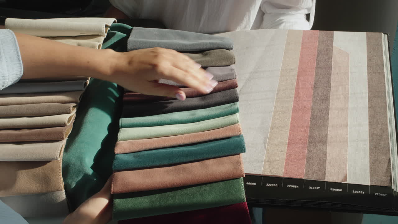 una mujer compradora recoge textiles en la tienda, compara la sombra con el catálogo de papel pintado. el vendedor tiene un álbum con muestras