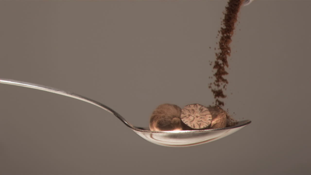 серебряная ложка заполнена в супер медленном движении с орехами и порошком, падающими на нее