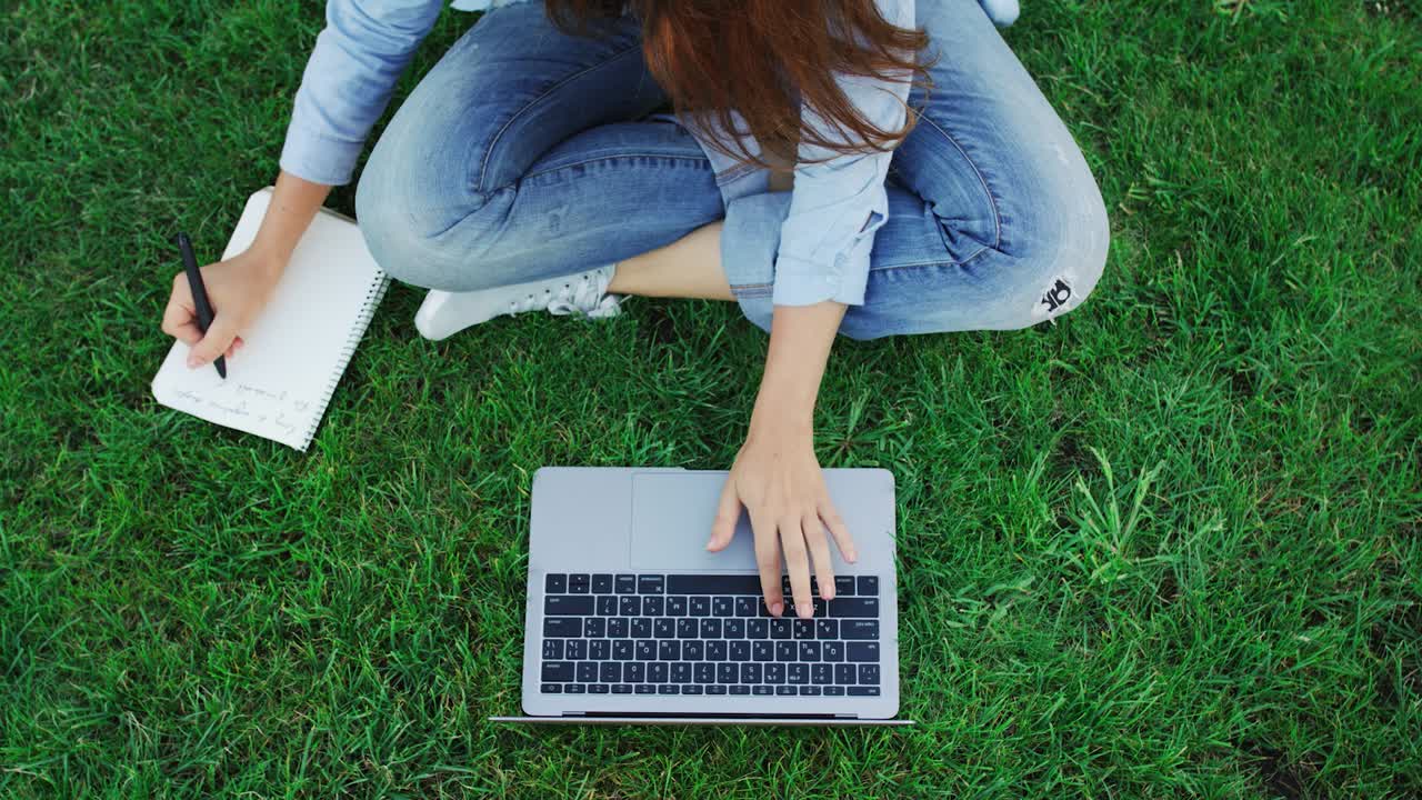 mujer estudiante trabajando en una computadora portátil y escribiendo notas en un cuaderno en el parque