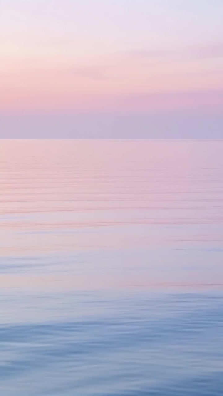 Vertical video: Glistening sea surface forming ripples from light breeze at low horizon, pastel sky