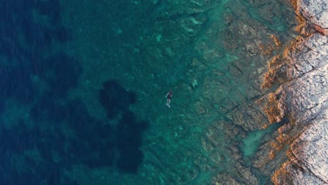 Man-snorkeling-in-the-pristine-turquoise-sea-with-healty-corals-and-rocks