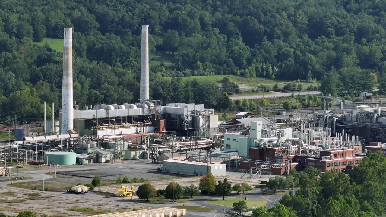 Industrial American factory with pipelines and smokestacks near forest landscape. Sunny day in industrial district of town. Aerial wide shot. Pollution of environment nature
