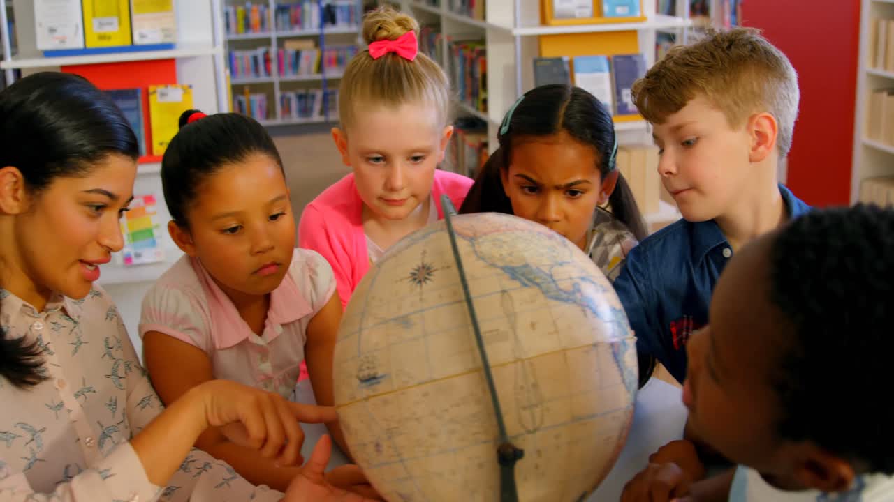 maestra asiática enseñando a los niños sobre el globo en la mesa en la biblioteca de la escuela 4k