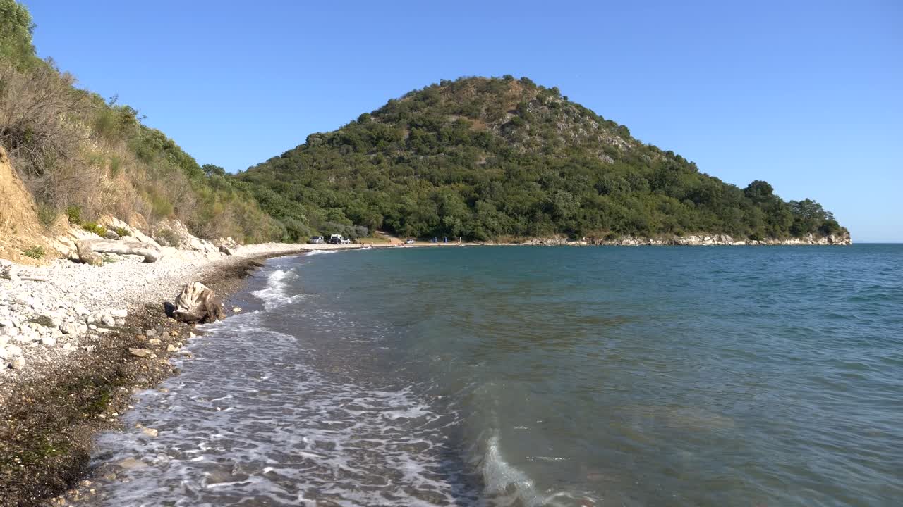 playa en grecia, las olas del mar jónico bañando una playa rocosa, con montañas en el fondo