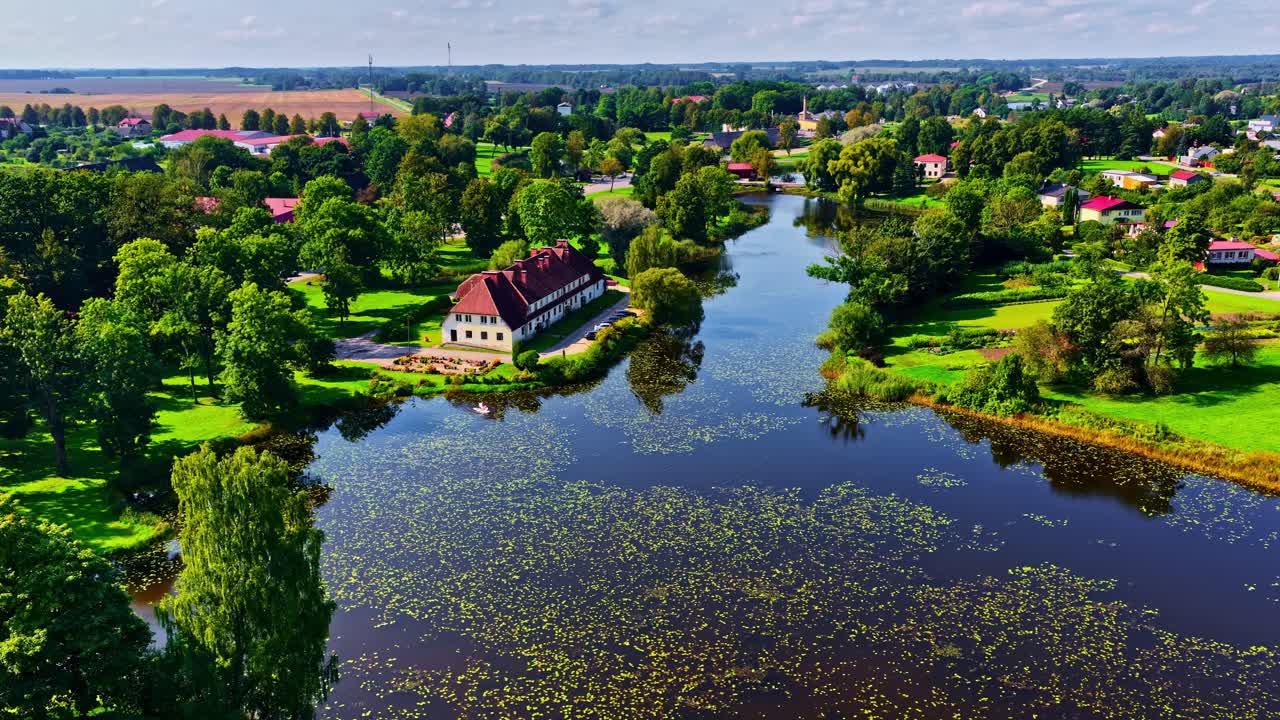 Aerial flies over Jaunpils Castle with river and surrounding landscape in bright sunlight, idyllic travel scene